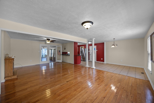 unfurnished living room featuring ceiling fan with notable chandelier, decorative columns, light hardwood / wood-style flooring, and plenty of natural light