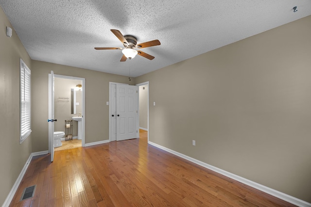 unfurnished bedroom with ceiling fan, multiple windows, light hardwood / wood-style flooring, and ensuite bath