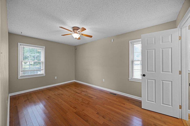 unfurnished room with a healthy amount of sunlight, ceiling fan, wood-type flooring, and a textured ceiling