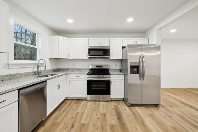 kitchen with light stone counters, stainless steel appliances, sink, light hardwood / wood-style flooring, and white cabinets