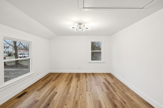 empty room featuring light hardwood / wood-style floors, vaulted ceiling, and a notable chandelier