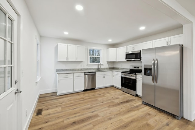 kitchen with sink, light stone countertops, light wood-type flooring, white cabinetry, and stainless steel appliances