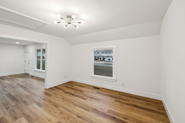 spare room featuring light hardwood / wood-style floors, vaulted ceiling, and an inviting chandelier