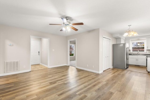 unfurnished living room with ceiling fan with notable chandelier, sink, and light hardwood / wood-style flooring