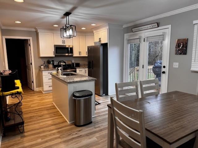 kitchen featuring light stone countertops, appliances with stainless steel finishes, a kitchen island with sink, white cabinets, and hanging light fixtures