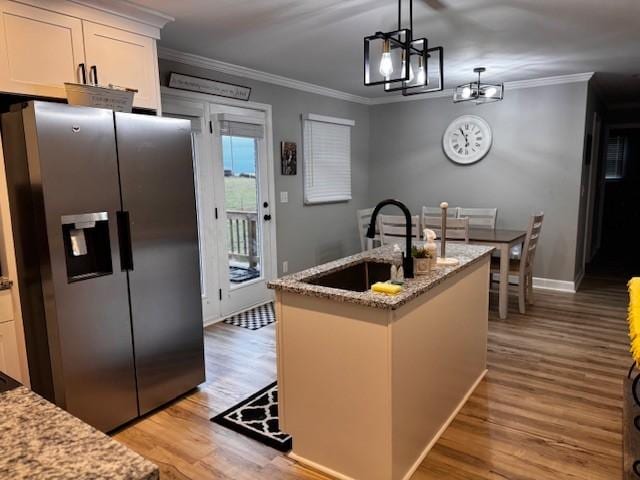 kitchen with stainless steel fridge, light stone countertops, an island with sink, decorative light fixtures, and white cabinetry