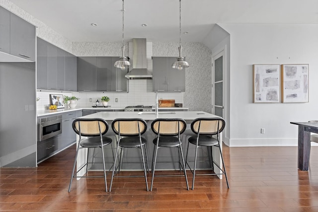 kitchen with backsplash, wall chimney exhaust hood, sink, gray cabinets, and an island with sink