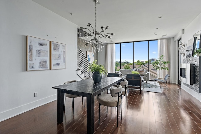 dining area featuring a fireplace, a chandelier, dark hardwood / wood-style floors, and a wall of windows