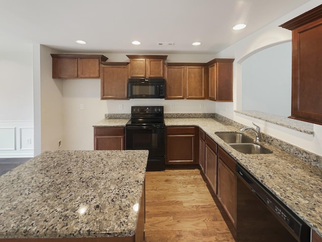 kitchen featuring light wood-type flooring, sink, light stone counters, and black appliances