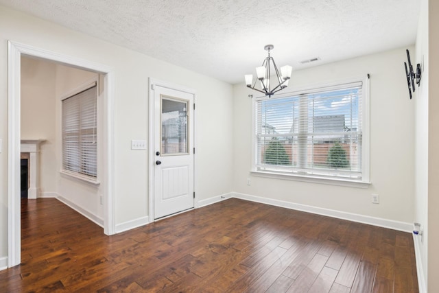 unfurnished dining area featuring a textured ceiling, dark hardwood / wood-style floors, and a chandelier