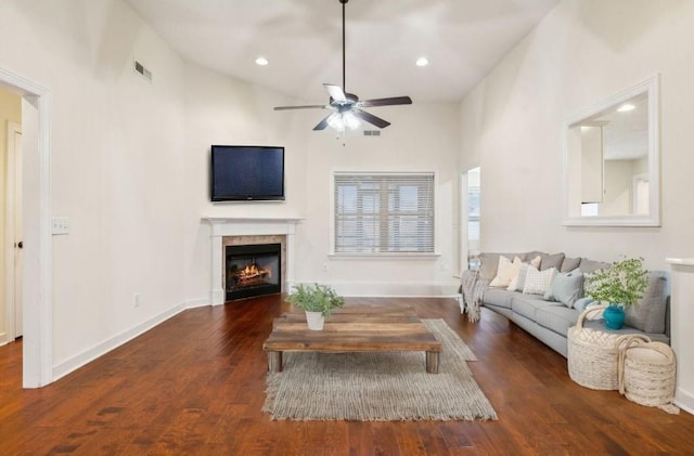 living room with ceiling fan, dark hardwood / wood-style floors, a tile fireplace, and a towering ceiling