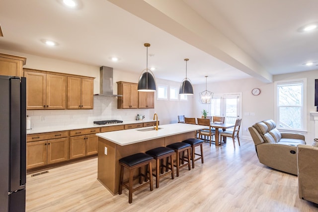 kitchen featuring wall chimney exhaust hood, black fridge, pendant lighting, a breakfast bar, and a center island with sink