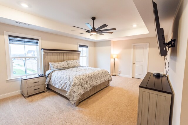 bedroom featuring light colored carpet, a raised ceiling, and ceiling fan