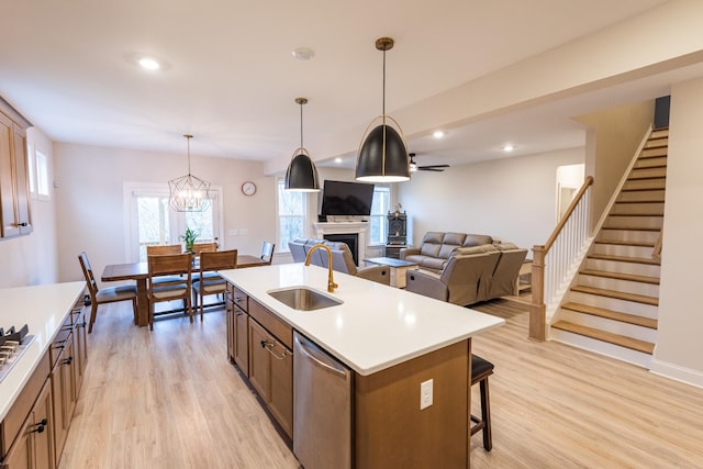 kitchen featuring sink, hanging light fixtures, stainless steel dishwasher, an island with sink, and light wood-type flooring