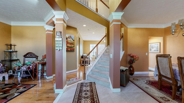 foyer with ornamental molding, light hardwood / wood-style flooring, a textured ceiling, and ornate columns