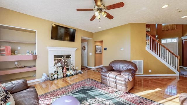 living room with a tiled fireplace, a textured ceiling, and light hardwood / wood-style flooring