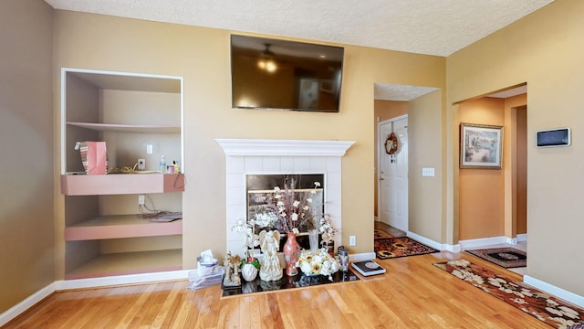 unfurnished living room with built in features, wood-type flooring, a tiled fireplace, and a textured ceiling