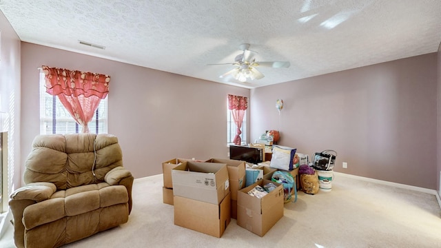 living area featuring ceiling fan, light carpet, and a textured ceiling