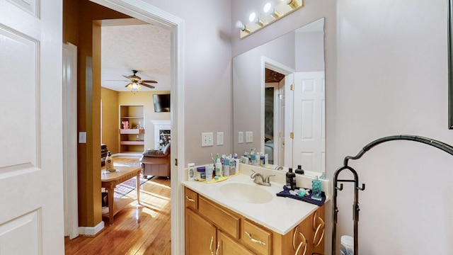 bathroom with built in shelves, a textured ceiling, vanity, ceiling fan, and hardwood / wood-style floors