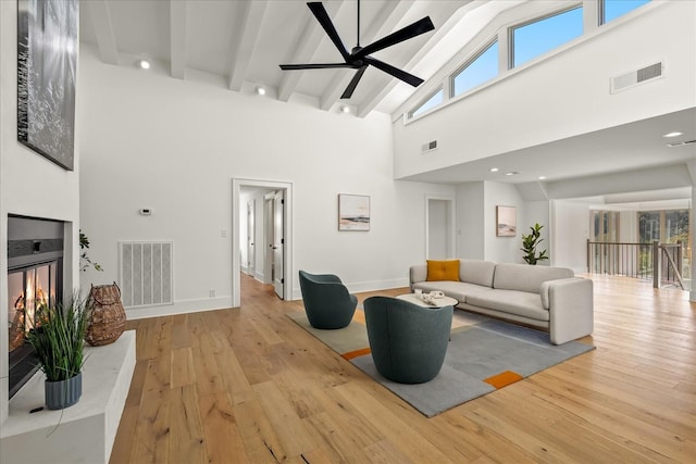 living room featuring beamed ceiling, light wood-type flooring, high vaulted ceiling, and ceiling fan