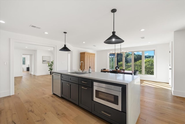 kitchen with a center island with sink, sink, appliances with stainless steel finishes, decorative light fixtures, and light hardwood / wood-style floors