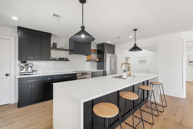 kitchen featuring a center island with sink, decorative backsplash, stainless steel appliances, and a breakfast bar