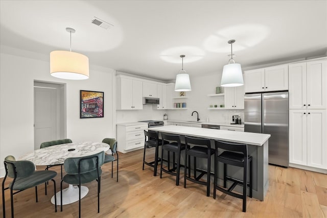 kitchen with decorative light fixtures, stainless steel appliances, and white cabinetry