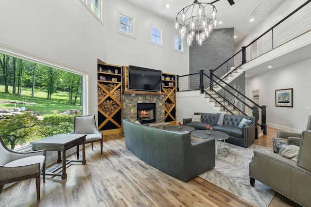 living room featuring a notable chandelier, light hardwood / wood-style floors, a stone fireplace, and a high ceiling