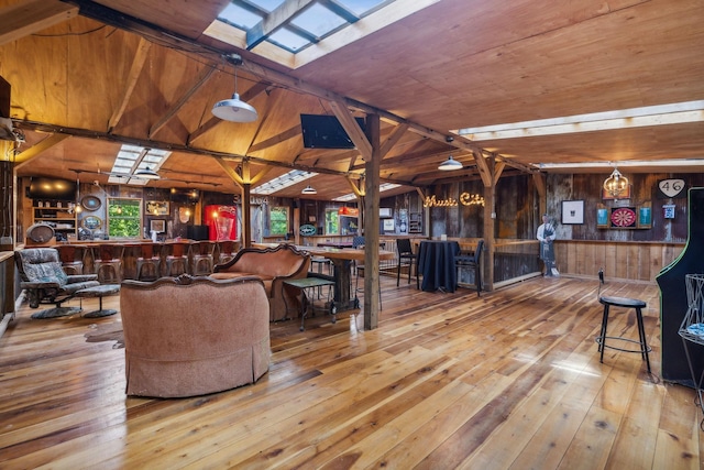 living room with vaulted ceiling with beams, wood walls, indoor bar, and hardwood / wood-style flooring