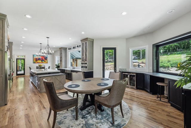 dining space featuring wine cooler, sink, light hardwood / wood-style flooring, and a notable chandelier