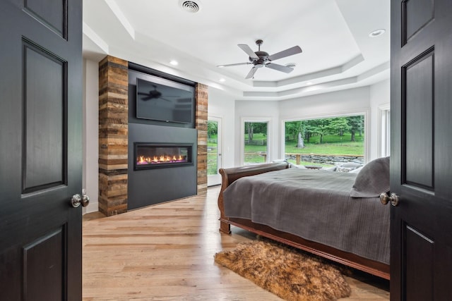 bedroom with a fireplace, light hardwood / wood-style floors, a raised ceiling, and ceiling fan