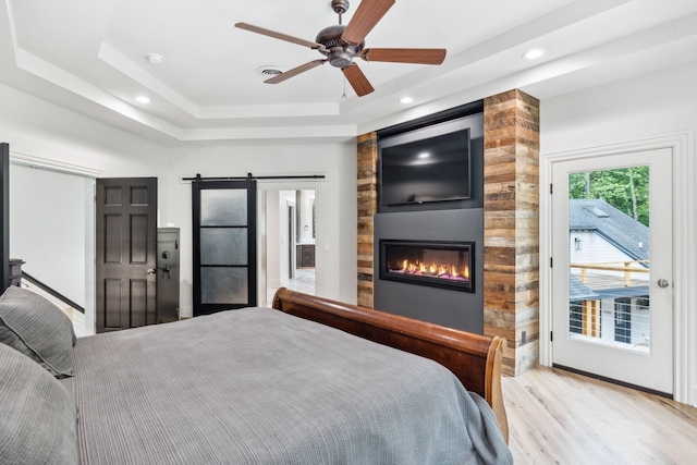 bedroom with access to outside, a raised ceiling, ceiling fan, a fireplace, and light hardwood / wood-style floors