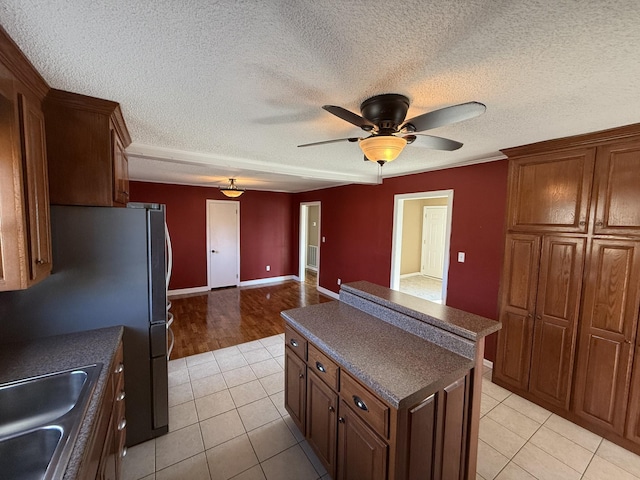 kitchen featuring ceiling fan, sink, light tile patterned floors, a textured ceiling, and a kitchen island