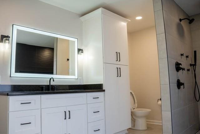 bathroom with a tile shower, vanity, and toilet