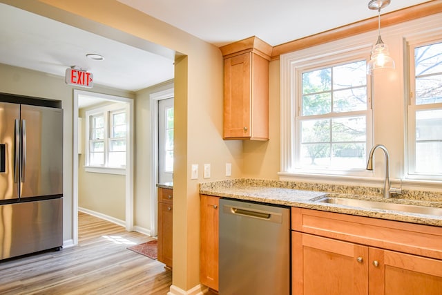 kitchen with appliances with stainless steel finishes, light stone counters, sink, pendant lighting, and light hardwood / wood-style floors