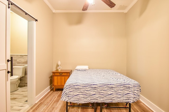 bedroom featuring ceiling fan, crown molding, a barn door, connected bathroom, and light hardwood / wood-style floors