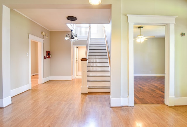 stairs with ornamental molding, ceiling fan with notable chandelier, and hardwood / wood-style flooring