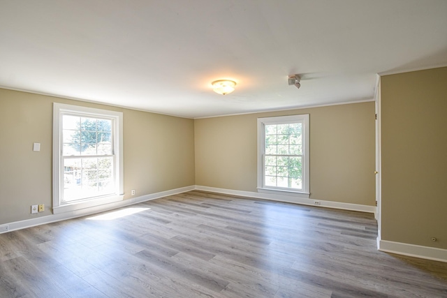 empty room with ornamental molding, light wood-type flooring, and a healthy amount of sunlight