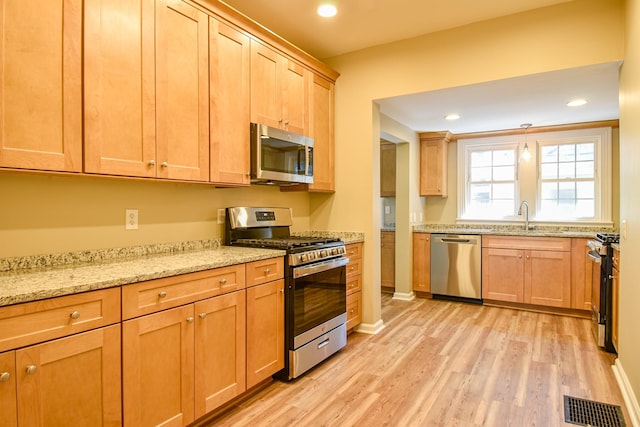 kitchen with light stone countertops, appliances with stainless steel finishes, light wood-type flooring, and sink