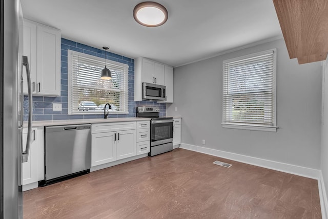 kitchen with decorative light fixtures, backsplash, stainless steel appliances, and white cabinetry