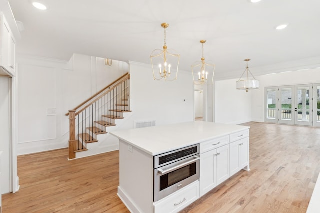 kitchen featuring crown molding, light hardwood / wood-style flooring, white cabinets, oven, and hanging light fixtures