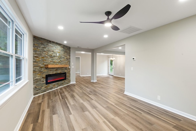 unfurnished living room featuring ceiling fan, light hardwood / wood-style floors, and a stone fireplace