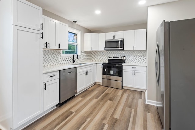 kitchen with white cabinetry, sink, stainless steel appliances, and decorative light fixtures