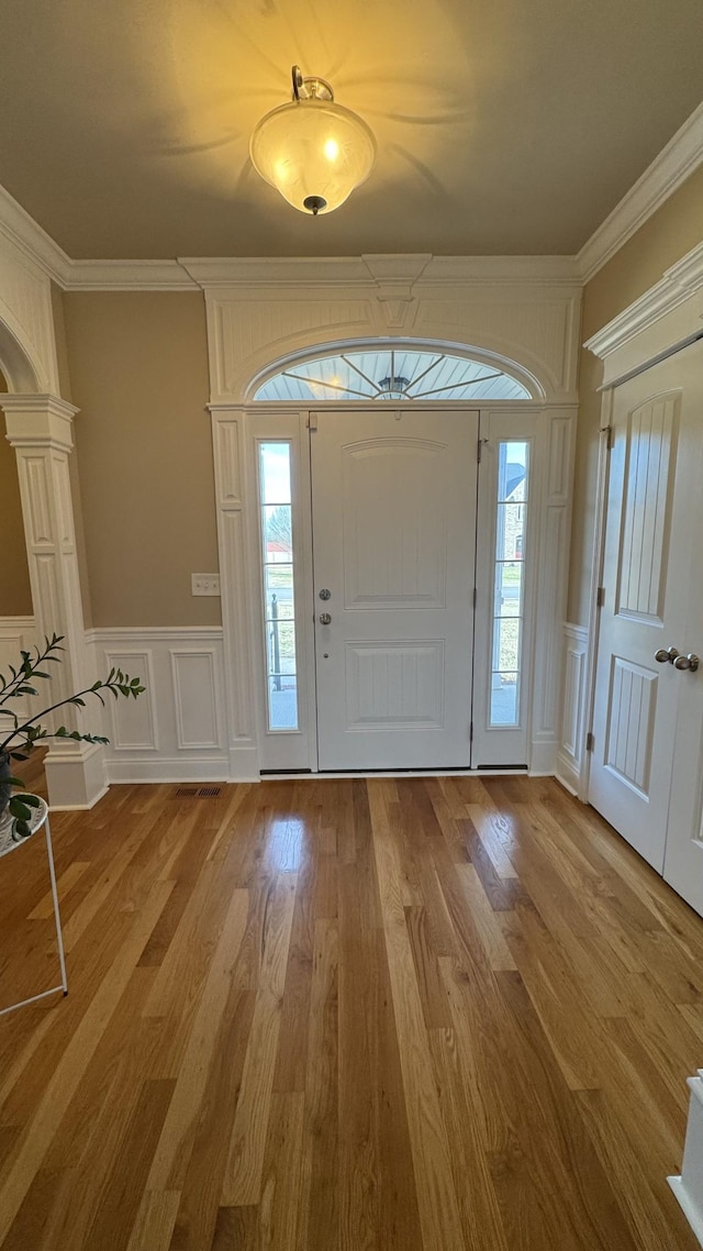 entryway with wood-type flooring, crown molding, and decorative columns