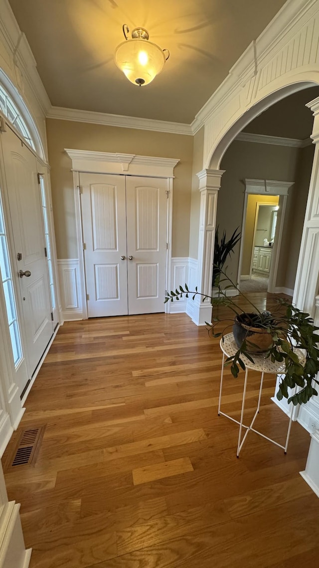 foyer entrance featuring hardwood / wood-style flooring, ornate columns, and crown molding