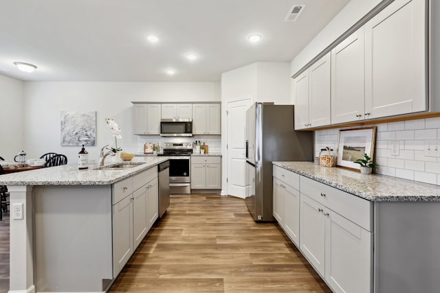 kitchen with sink, stainless steel appliances, light stone counters, light hardwood / wood-style floors, and decorative backsplash