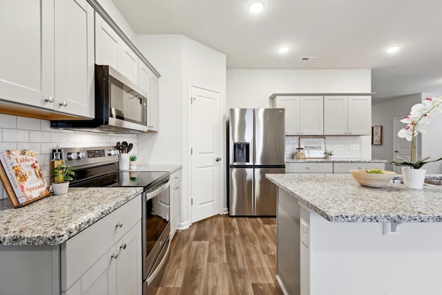 kitchen featuring decorative backsplash, appliances with stainless steel finishes, light stone counters, and hardwood / wood-style floors