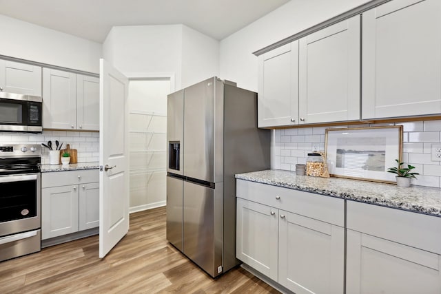 kitchen with light stone countertops, decorative backsplash, stainless steel appliances, and light hardwood / wood-style flooring