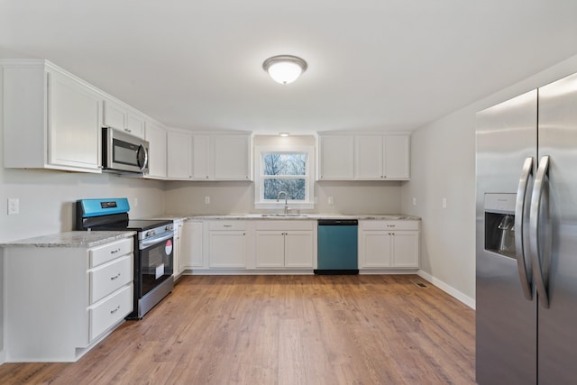 kitchen featuring light stone countertops, light wood-type flooring, stainless steel appliances, sink, and white cabinets