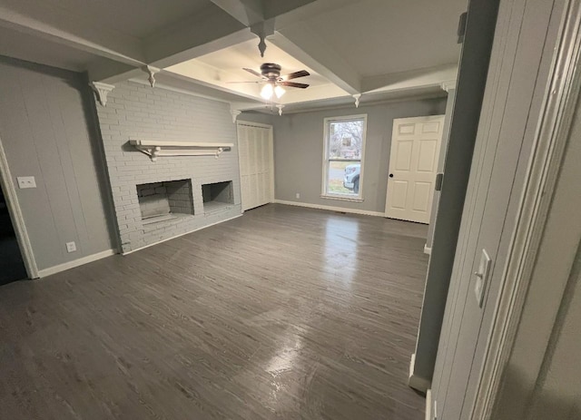 unfurnished living room with beamed ceiling, a brick fireplace, ceiling fan, and dark wood-type flooring